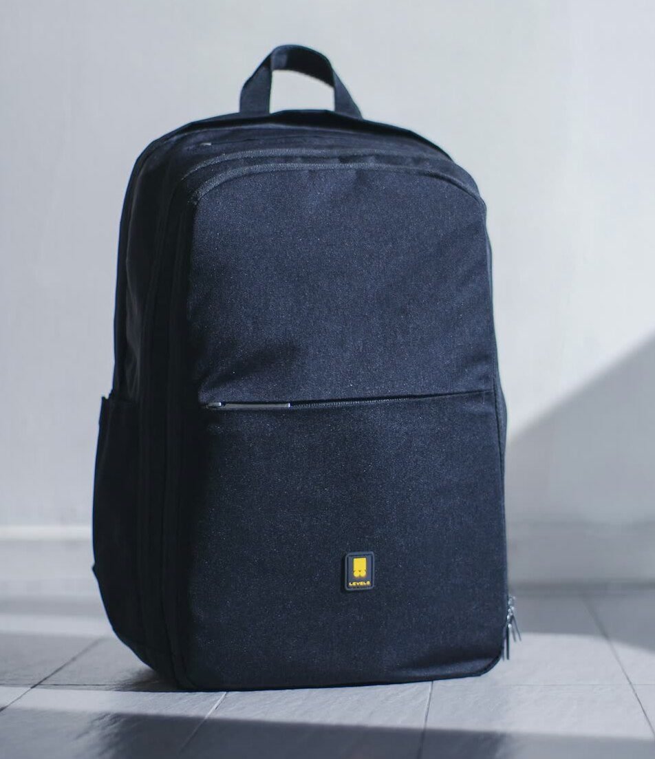 A charcoal backpack standing against a pale wall